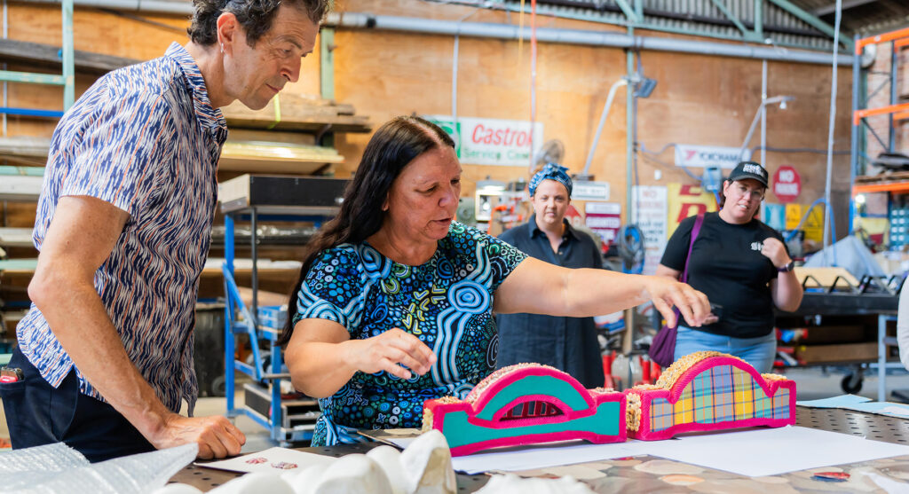 Aunty Lola Ryan, City People and Pink Cactus team inspecting original shell harbour bridges made by artist’s mother, 2025, Rockdale, Sydney; photo: DCITHS

This project is proudly funded by the NSW Government's Community Improvement District Pilot Program and Uptown Grant Program.